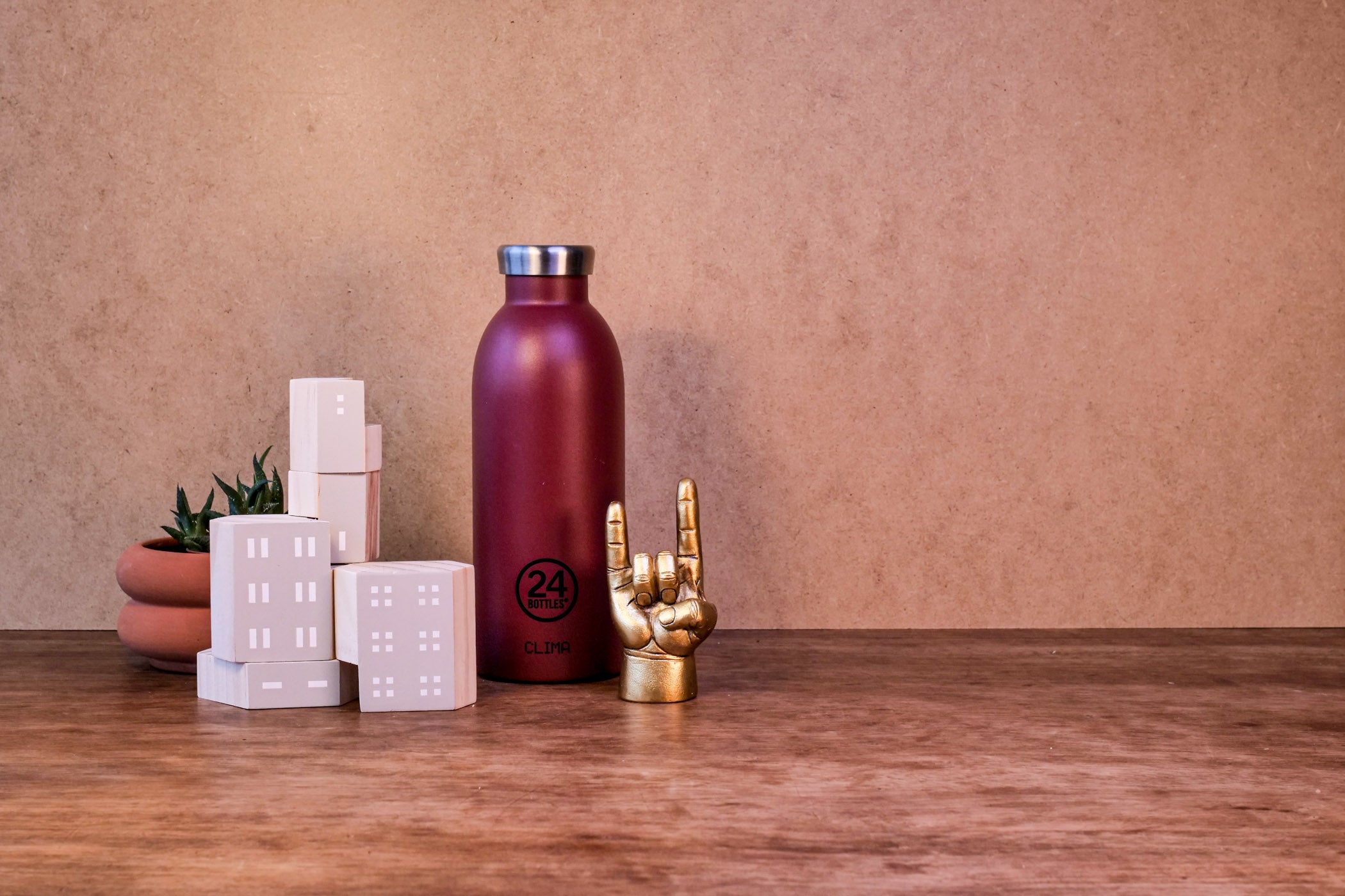 Wooden table with a plant in a ceramic pot, wooden building blocks, a red water bottle and a small gold statue of a hand making devil horns