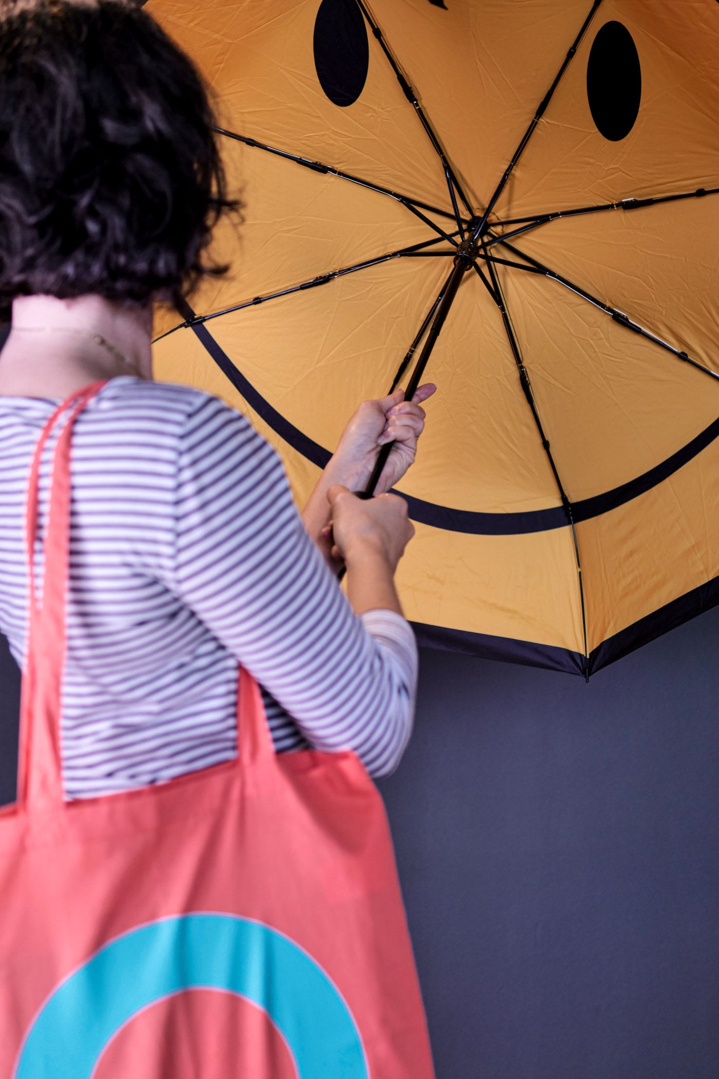 Woman holding an open umbrella with a yellow smiley face inside