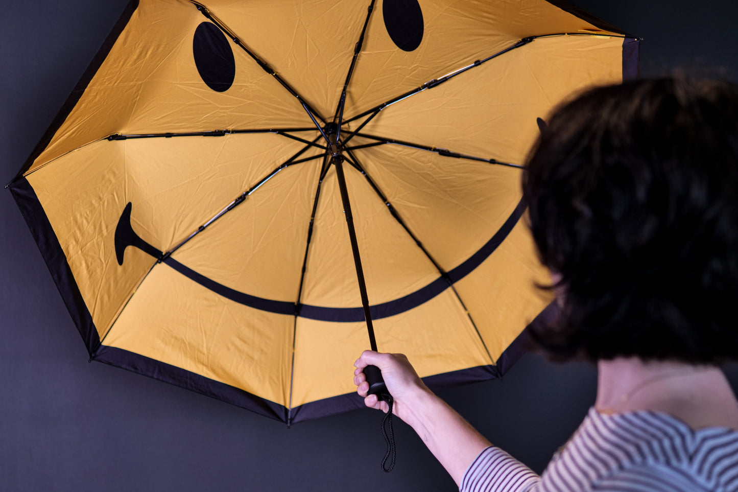 Woman holding an open umbrella with a yellow smiley face inside