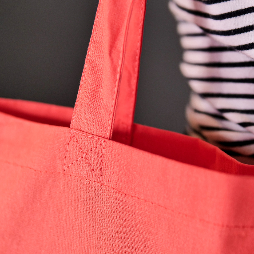 Close up of Bright coral canvas bag featuring the DLWP roundel in aqua blue