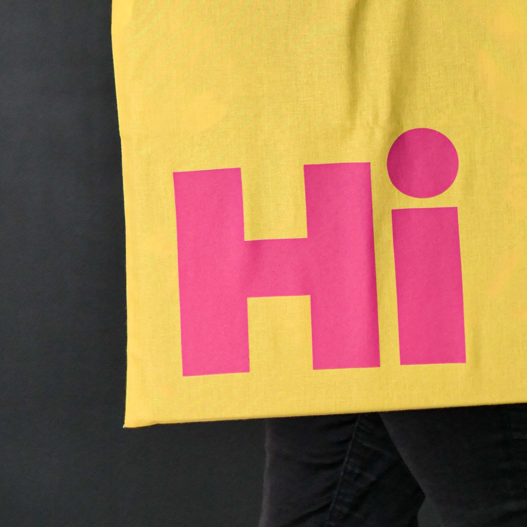 close up of Hi in bright pink large font on the yellow tote bag