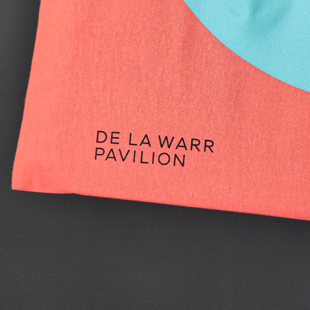 close up of Bright coral canvas bag featuring the DLWP roundel in aqua blue