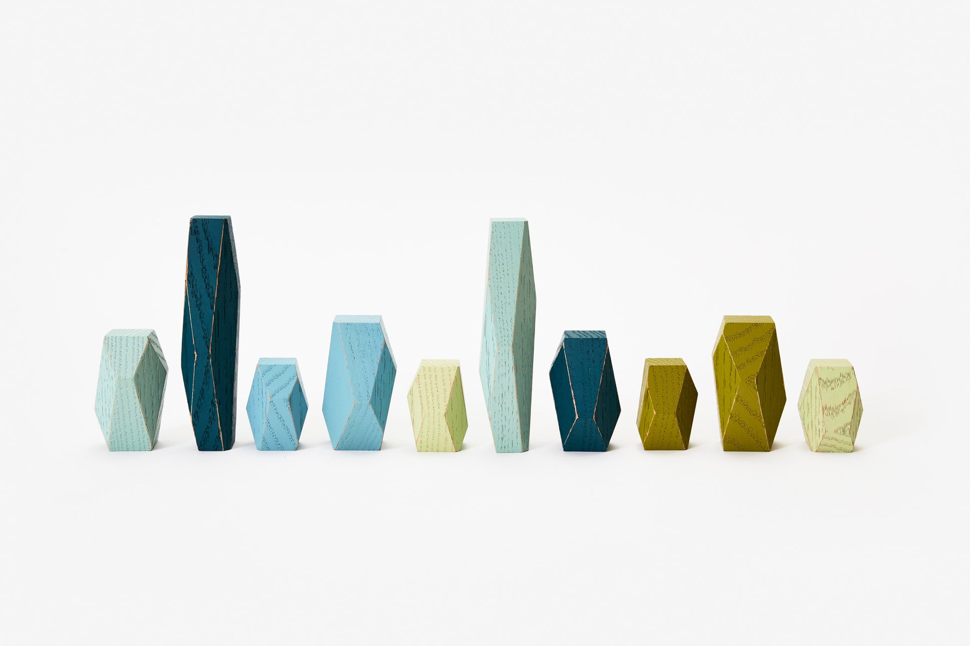 Faceted wooden shapes in various shades of blue and green, in a row.