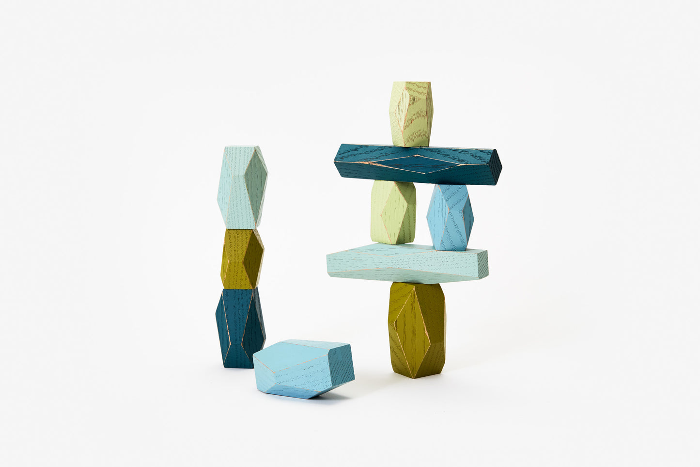 Faceted wooden shapes in various shades of blue and green, balanced on top of each other.
