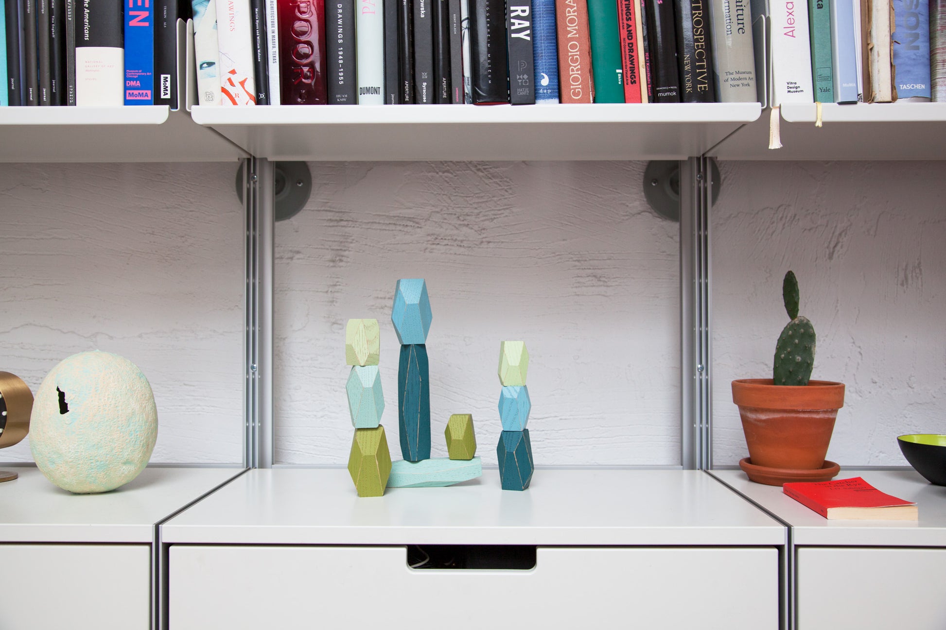Faceted wooden shapes in various shades of blue and green, on a white desk.