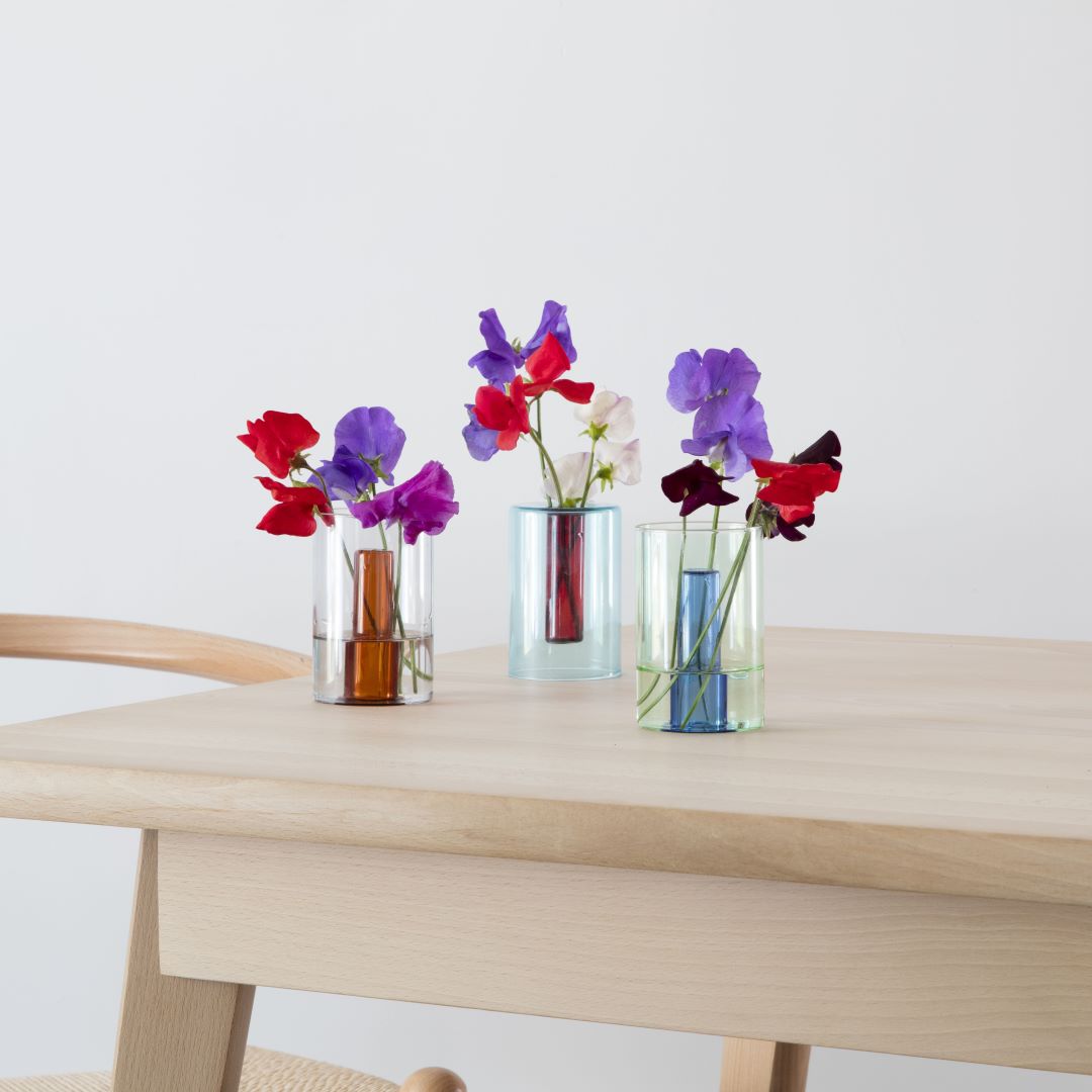 three reversible coloured glass vases with sweet pea flowers on a wooden table
