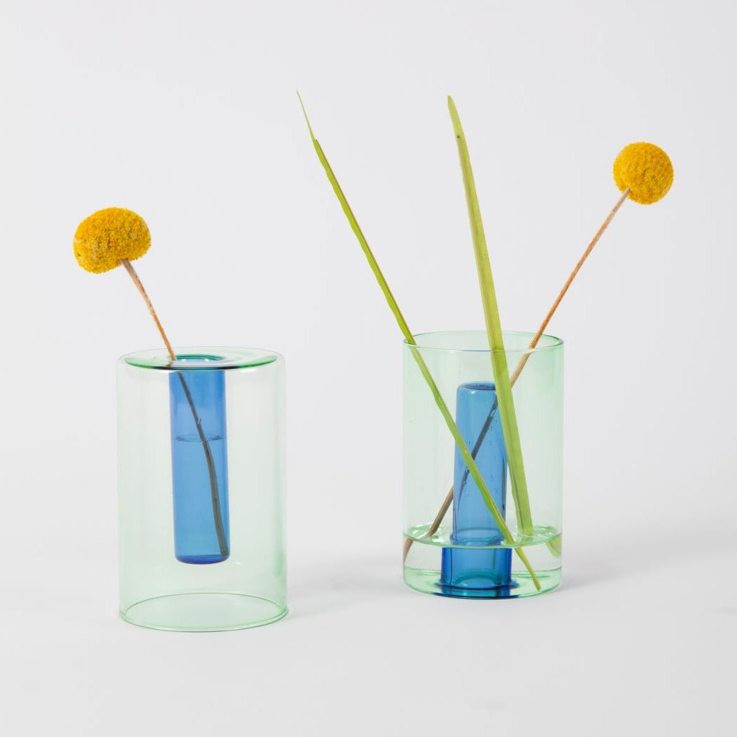 Two green and blue reversible vases with yellow flower stems