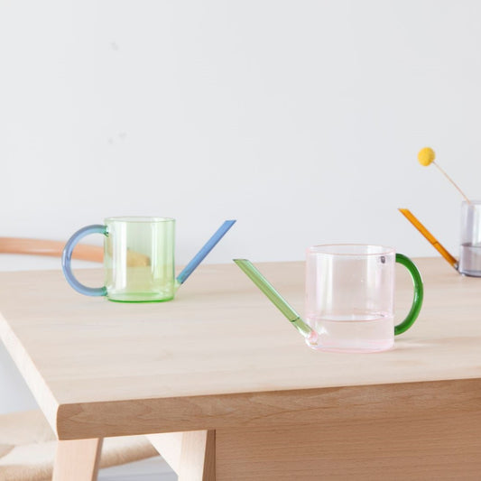 Three glass watering cans on a wooden table.