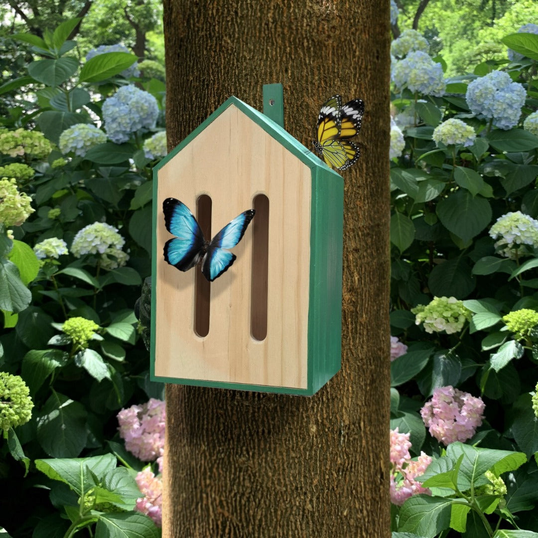 Butterfly house in front of a tree with two butterflies nearby.