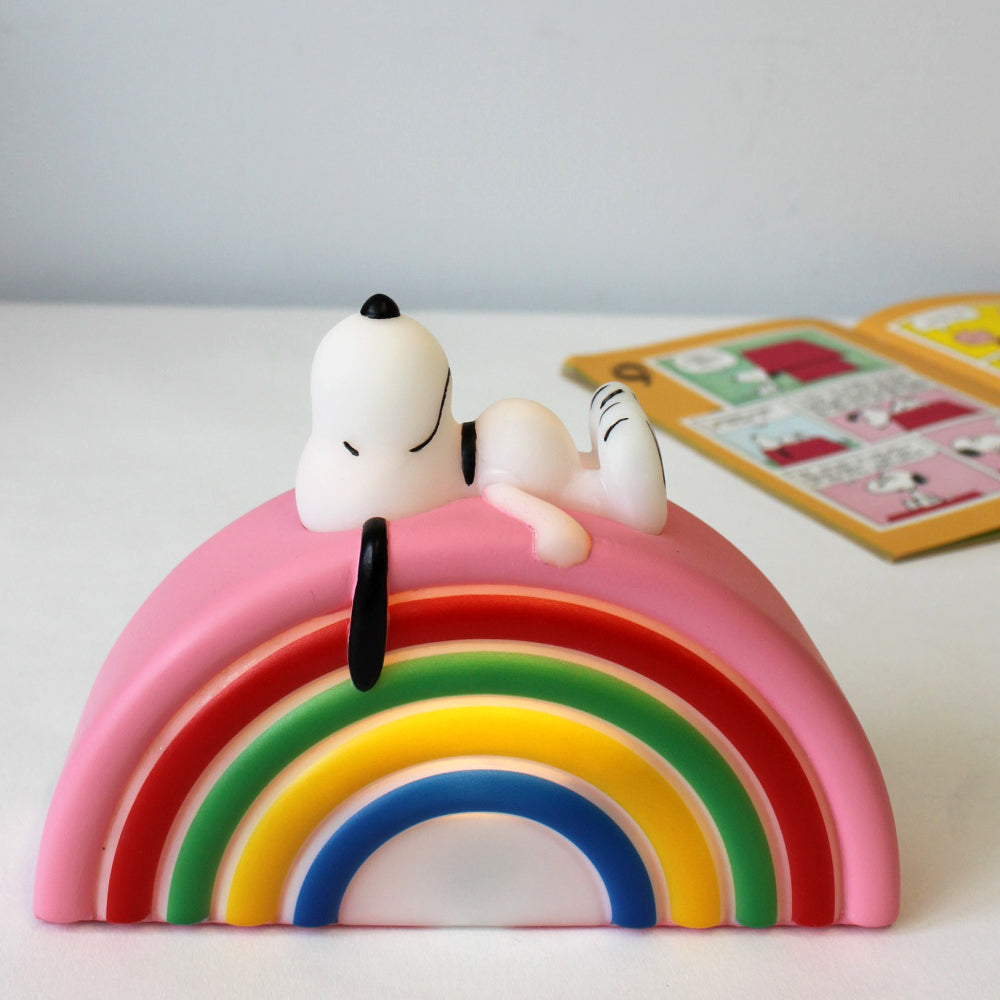 Lamp in the shape of a rainbow, with Snoopy lying on top. A Peanuts comic is in the background.