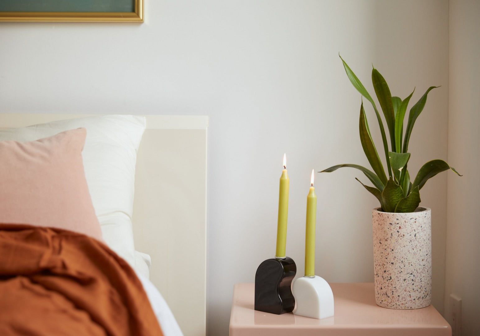 curved black and white candle holders which fit together on a bedside table- two lit green candles are in them