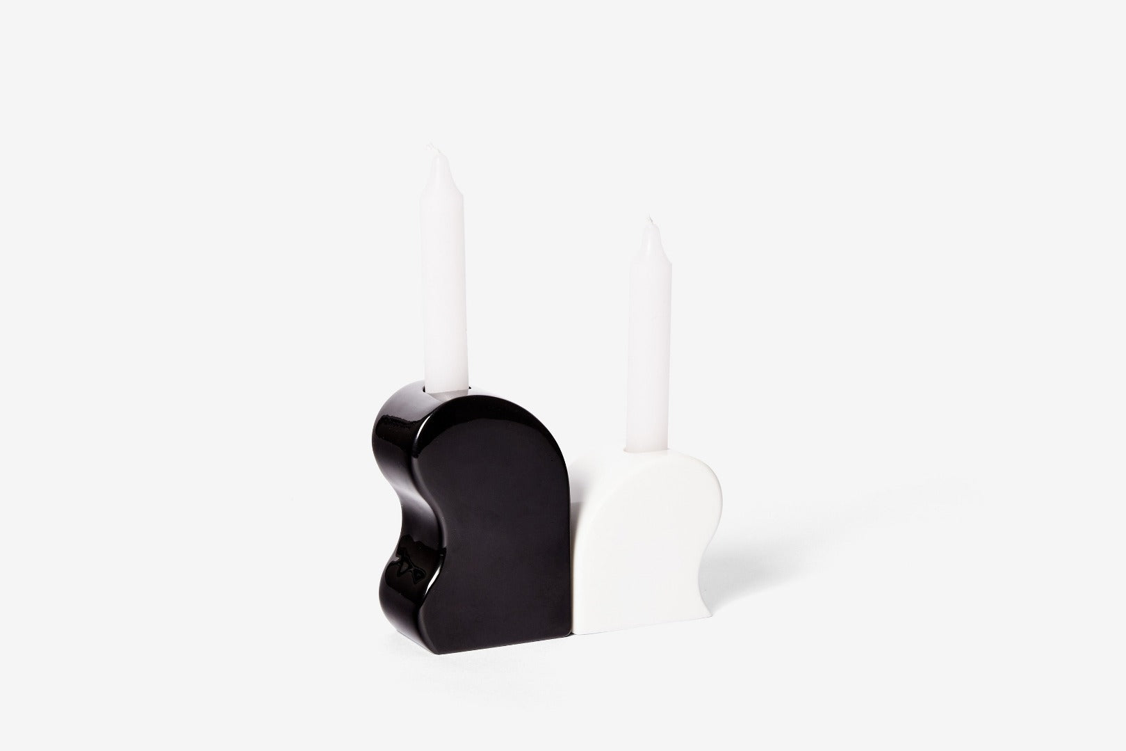 curved black and white candle holders facing away from each other - two unlit white candles are in them